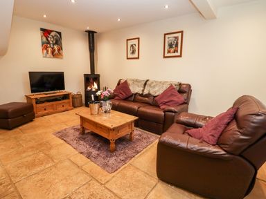 A living room with leather sofas a wooden coffee table a television and a wood burning stove at The Stables in Great Tew near Chipping Norton