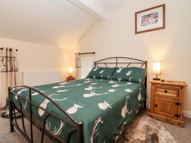 A bedroom with a metal bed frame and green bedding with deer head prints next to wooden bedside tables with lamps at The Stables Great Tew near Chipping Norton
