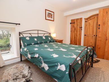A bedroom with a metal bed frame a green duvet with white deer heads wooden bedside table wooden door and wardrobe and a small window at The Stables in Great Tew near Chipping Norton