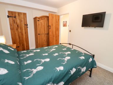 A bedroom with a bed with green bedding a wooden wardrobe wooden doors and a wall-mounted television at The Stables Great Tew near Chipping Norton