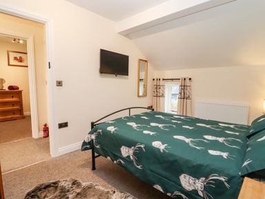A bedroom with a bed covered in green bedding with white deer prints and a wall-mounted TV at The Stables in Great Tew near Chipping Norton