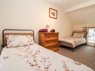 A bedroom with two single beds a wooden chest of drawers and a window at The Stables in Great Tew near Chipping Norton