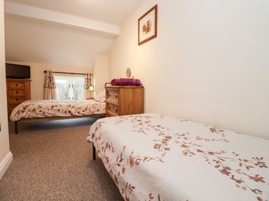 A bedroom with two beds a wooden chest of drawers and a window at The Stables in Great Tew near Chipping Norton