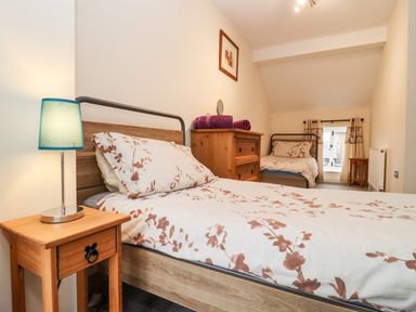 A bedroom with two single beds wooden bedside table with lamp wooden dresser and window with curtains at The Stables in Great Tew near Chipping Norton