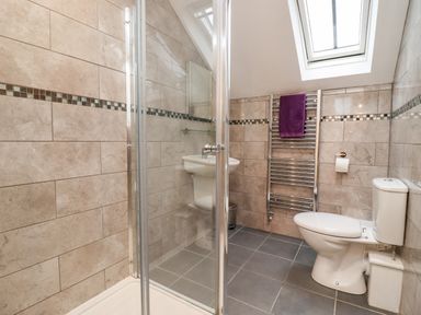 A bathroom with a shower, toilet, sink, and heated towel rail with a purple towel at The Stables in Great Tew near Chipping Norton