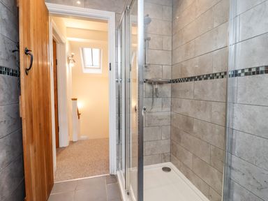A bathroom with a tiled walk-in shower and a wooden door open to a carpeted hallway at The Stables in Great Tew near Chipping Norton
