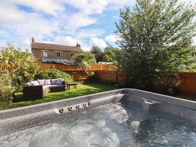 A garden with a hot tub a sofa an outdoor table and a tree at The Stables in Great Tew near Chipping Norton