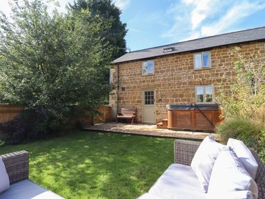 A garden with a lawn bench hot tub and stone house at The Stables in Great Tew near Chipping Norton
