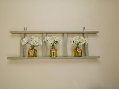 Three small green glass jars with white flowers on a green wooden wall shelf at Ericas eaven Farndale near Kirkbymoorside