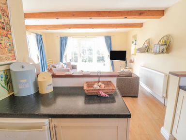 A kitchen counter with a bread bin and biscuit tin overlooking a living room with blue curtains and a television at Ericas eaven in Farndale near Kirkbymoorside