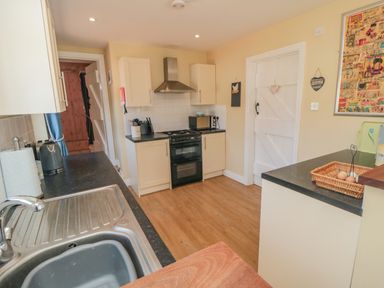A kitchen with a sink, stove, microwave, cabinets, and wooden flooring at Ericas Heaven in Farndale near Kirkbymoorside