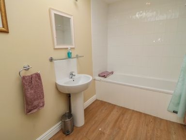 A bathroom with a pedestal sink below a small mirror a towel ring with a towel a bathtub with folded towels and wood effect flooring at Ericas eaven in Farndale near Kirkbymoorside