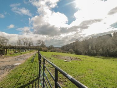 A green field with a metal gate and a dirt road under a partly cloudy sky at Ericas eaven in Farndale near Kirkbymoorside