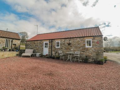 A stone cottage with a red tiled roof and outdoor seating on a gravel area at Ericas eaven in Farndale near Kirkbymoorside
