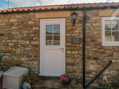 A stone house exterior with a white door and window and a sign reading Ericas eaven at Farndale near Kirkbymoorside