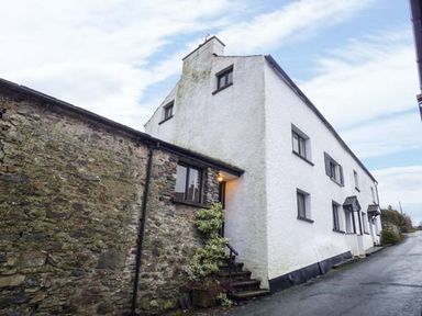A white two story house with black window frames and a stone wall next to a road at High House Newton in Cartmel near Cartmel