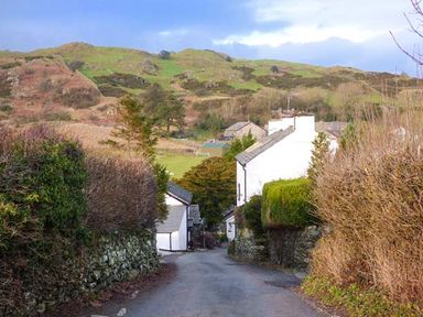 A narrow road lined with hedges and white houses with hills in the background at High House in Newton in Cartmel near Cartmel
