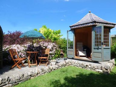 A garden with a stone patio table and chairs with an umbrella and a small wooden gazebo with open doors at High House Newton in Cartmel near Cartmel