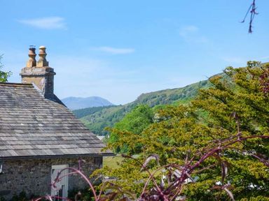 A rooftop with chimneys and trees with hills in the background at High House in Newton in Cartmel near Cartmel