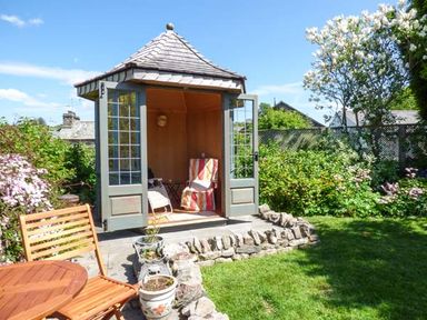 A garden gazebo with open doors and seating surrounded by plants and lawn at High House in Newton in Cartmel near Cartmel