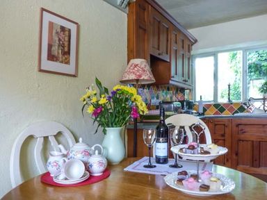 A kitchen with wooden cabinets flowers on a table tea set wine bottle and sweets on High House Newton in Cartmel near Cartmel