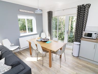 A dining area with a wooden table and six white chairs next to a gray sofa and glass doors at Wysteria Cottage in Windermere