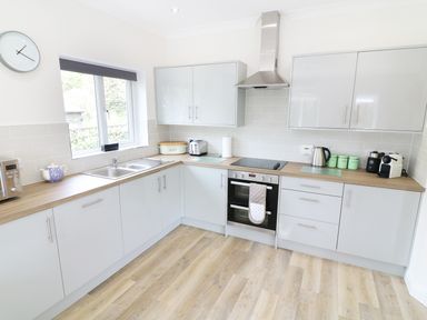 A kitchen with light gray cabinets wooden countertop stainless steel oven and hood and a window at Wysteria Cottage in Windermere