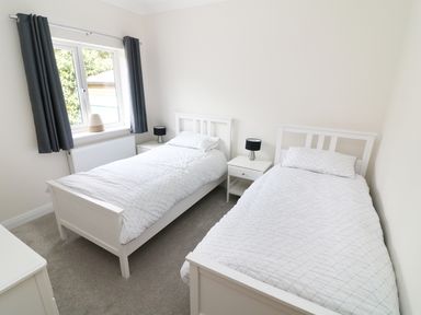 A bedroom with two single beds white bedding two small bedside tables with lamps and a window with dark curtains at Wysteria Cottage in Windermere
