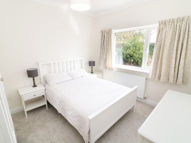 A bedroom with a white double bed two bedside tables with lamps a window with curtains and a radiator at Wysteria Cottage in Windermere