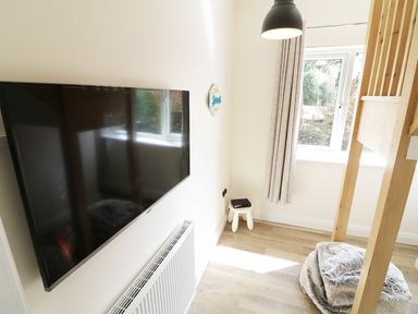A room with a wall-mounted TV radiator stool window curtain and a bunk bed at Wysteria Cottage in Windermere