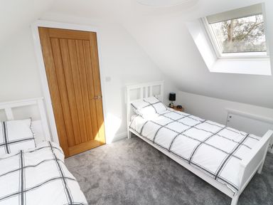 A bedroom with two single beds and a wooden door with a skylight window at Wysteria Cottage in Windermere