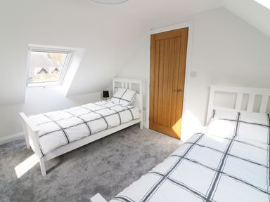A bedroom with two single beds a wooden door and a skylight window at Wysteria Cottage in Windermere
