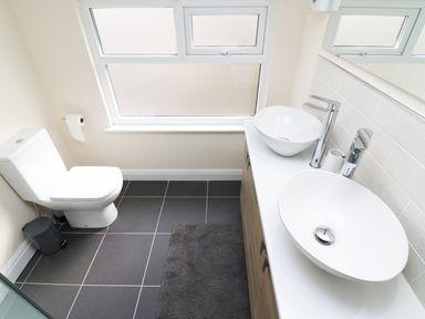A bathroom with a toilet a dual sink vanity and a window at Wysteria Cottage in Windermere