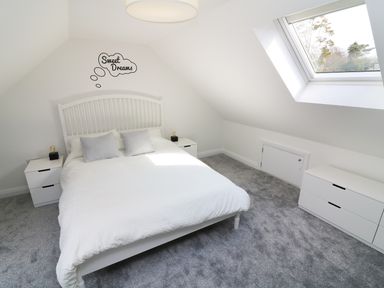A bedroom with a white bed and two side tables under a skylight window at Wysteria Cottage in Windermere