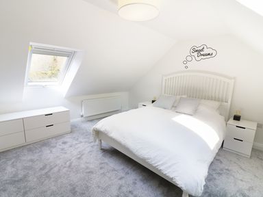 A bedroom with a white bed two bedside tables and a chest of drawers under a skylight window at Wysteria Cottage in Windermere