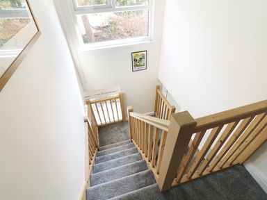 A stairway with wooden railings and grey carpet leading to a window with a framed picture on the wall at Wysteria Cottage in Windermere