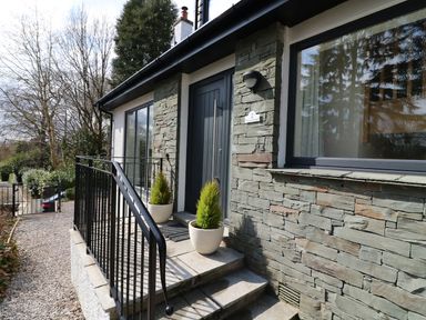 Front entrance of a building with stone walls a black door metal handrails and two potted plants at Wysteria Cottage in Windermere