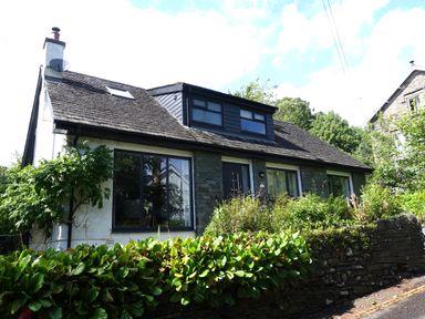 A residential house with a sloped roof and multiple windows surrounded by greenery at Wysteria Cottage in Windermere