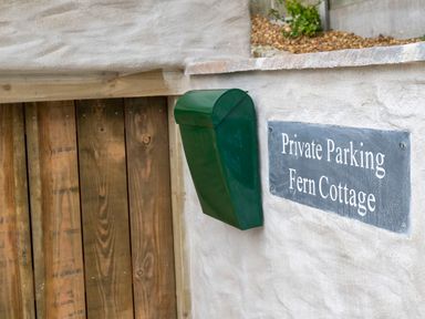 A private parking sign and green mailbox on a white wall near a wooden gate at Fern Cottage in Aberporth