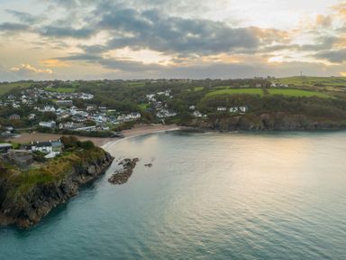 A coastal village with houses and green fields beside a bay with cliffs and a sandy beach at Fern Cottage in Aberporth