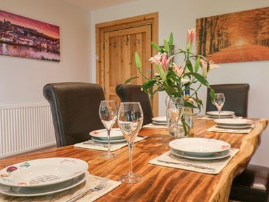 A dining table set with plates, wine glasses, cutlery, and a vase with flowers at Pond Farm Woodlands in Ugthorpe
