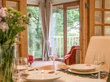 A dining table set with plates and glasses near a glass door leading to a balcony with chairs and trees visible at Pond Farm Woodlands in Ugthorpe