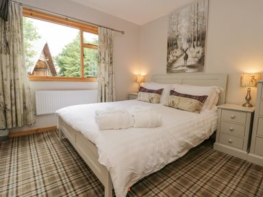 A bedroom with a bed and white linens two lamps on bedside tables and a window showing greenery at Pond Farm Woodlands in Ugthorpe