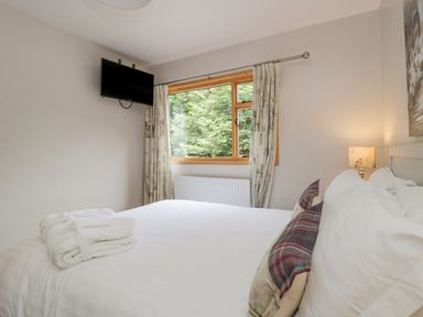 A bedroom with a bed a window a wall-mounted television and a bedside lamp at Pond Farm Woodlands in Ugthorpe