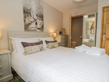 A bedroom with a double bed white bedding and pillows bedside tables with lamps a dresser and an open door showing a bathroom at Pond Farm Woodlands in Ugthorpe