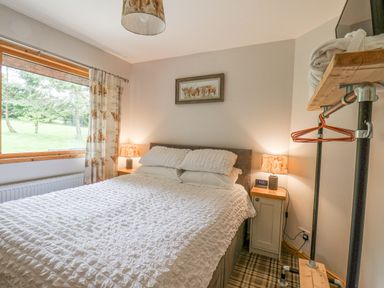 A bedroom with a double bed and bedside tables with lamps near a window with patterned curtains at Pond Farm Woodlands in Ugthorpe