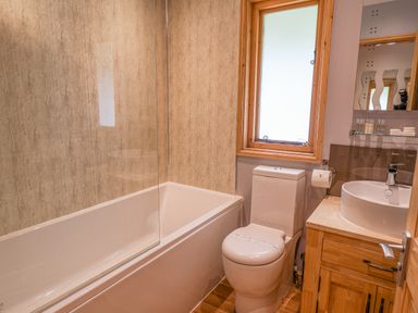 A bathroom with a bathtub a toilet a wooden cabinet with a sink and a frosted window at Pond Farm Woodlands in Ugthorpe