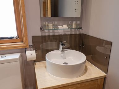A bathroom sink with toiletries on a glass shelf above and a window to the left at Pond Farm Woodlands in Ugthorpe