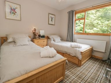 A bedroom with two single beds a wooden nightstand with a lamp and window with grey curtains at Pond Farm Woodlands in Ugthorpe