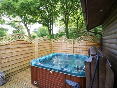 A hot tub on a wooden deck with a wooden privacy fence and trees at Pond Farm Woodlands in Ugthorpe